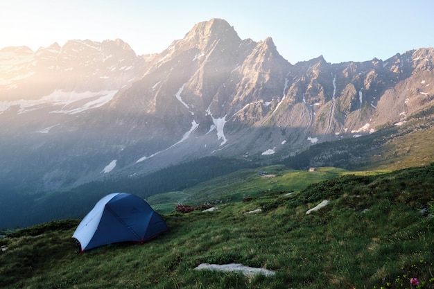 blue tent on a grassy hill with mountains and clear sky