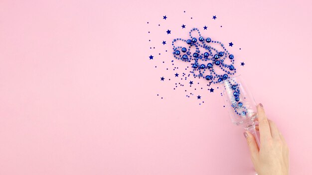 Blue tinsel in a glass on pink copy space background and hand