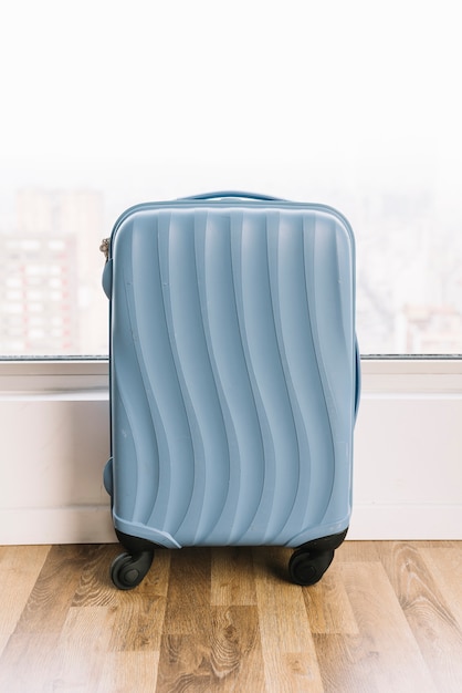 Free Photo blue travel suitcase near the window on wooden floor