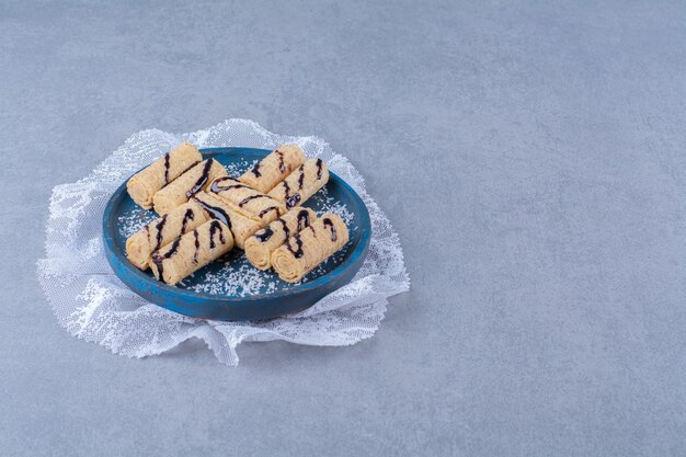 A blue wooden board of sweet sticks with sprinkles and chocolate syrup . 