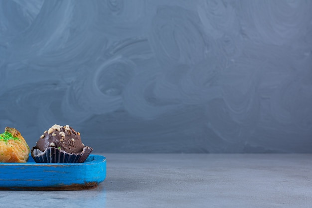 A blue wooden board of two chocolate cupcakes and baklawa .