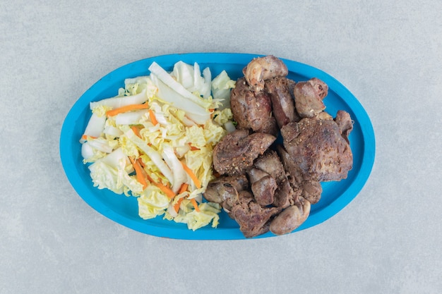 A blue wooden plate of fried meat and vegetable salad . 