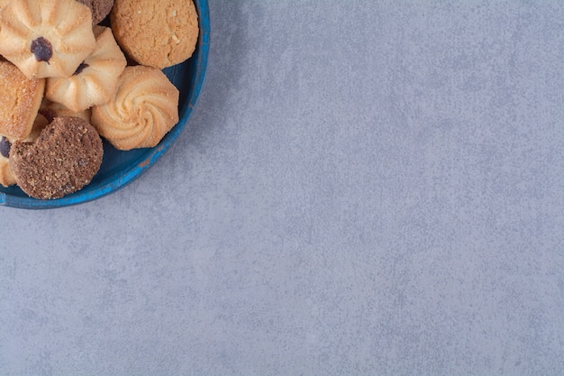 A blue wooden plate with sweet different cookies . 