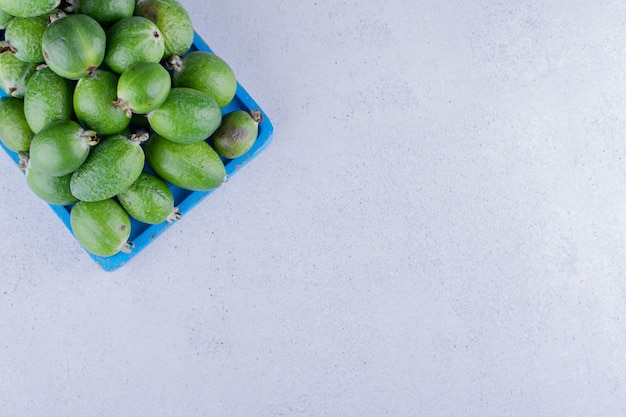 Free photo blue wooden platter stocked with a heap of feijoas on marble background. high quality photo