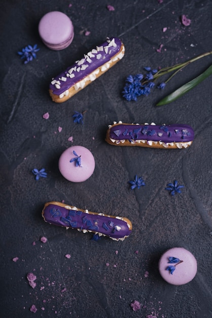 Free photo blueberry purple eclair with macaroons on black textured background