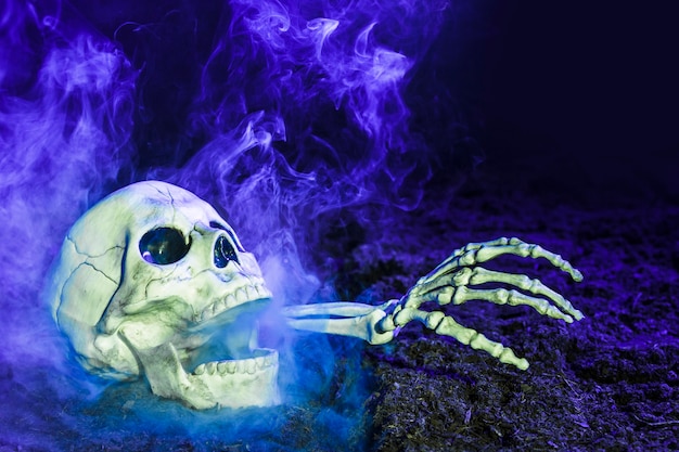 Free photo blueness skeleton's hand sticking out of skull on ground