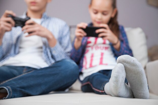 Blurred siblings playing video game and using smartphone