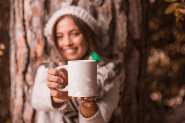 Blurred woman showing mug near tree