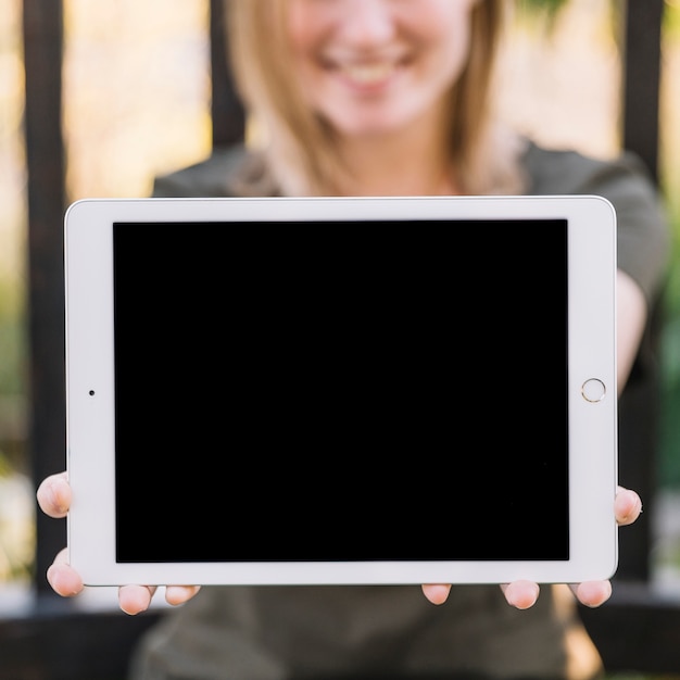 Free photo blurred woman showing tablet near fence