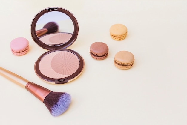 Blusher with macaroon and makeup brush on beige background