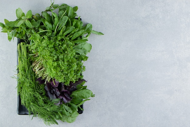 Board full of different greenery , on the marble background.