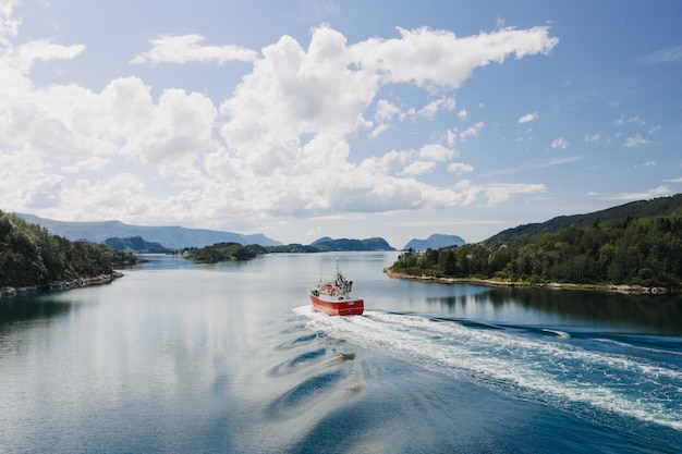 Free Photo a boat on the body of the water surrounded by trees under a clear blue sky with white clouds