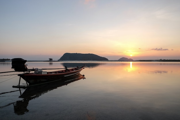 Free photo boat on the sea surrounded by hills with the sun reflecting on the water during the sunset