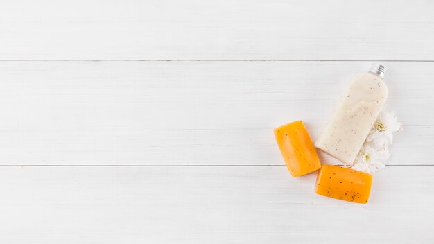 Body scrub bottle; herbal soap and white flower on wooden plank background