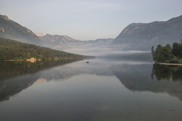 Free Photo body of water near mountain ranges with green vegetation covered with fog during daytime