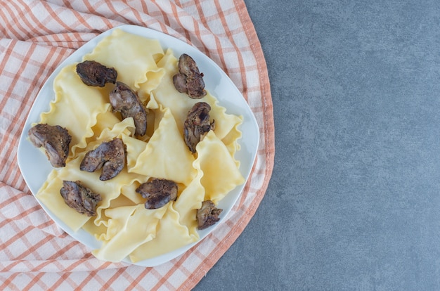 Boiled dough with dried meat parts on white plate.