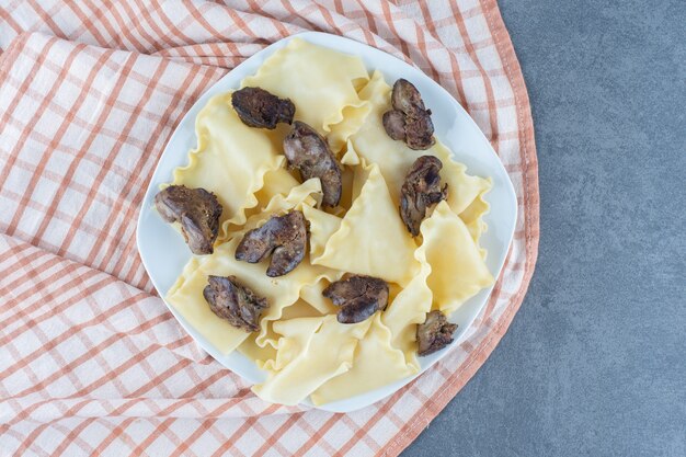 Boiled dough with dried meat parts on white plate. 