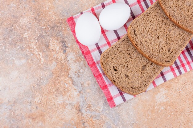 Boiled egg and bread on a tea towel, on the marble background.