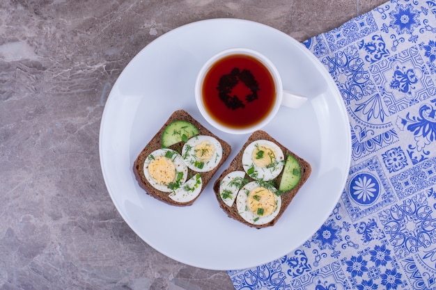 Boiled egg sandwich with a cup of tea in a white plate.