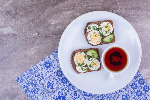 Boiled egg sandwich with a cup of tea in a white plate.