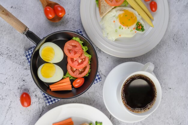 Boiled eggs, carrots, and tomatoes on a pan with tomato on a wooden spoon and coffee cup.