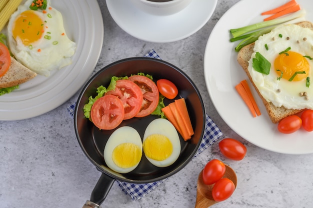 Boiled eggs, carrots, and tomatoes on a pan with tomato on a wooden spoon.