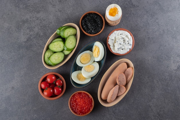 Free photo boiled eggs with fresh cucumber and red cherry tomatoes placed on stone table.