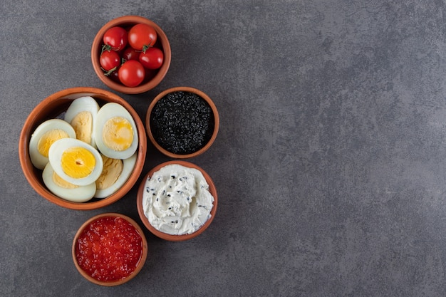 Free photo boiled eggs with red and black caviar placed on a stone background .