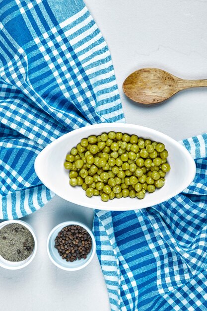 Boiled green peas in a white bowl with spices, a spoon, and a tablecloth.