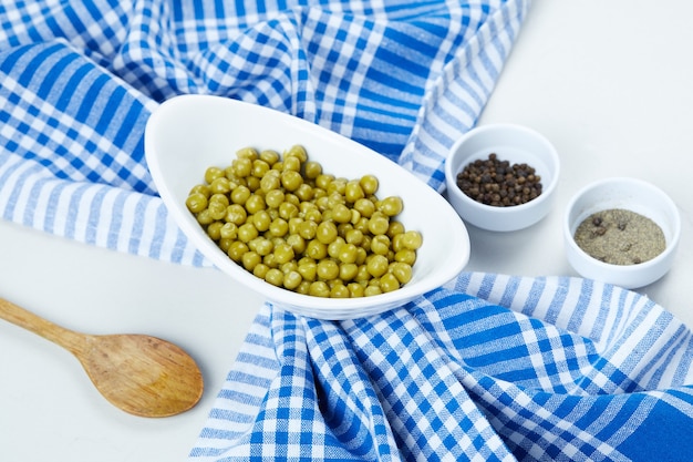 Boiled green peas in a white bowl with spices, a spoon, and a tablecloth.