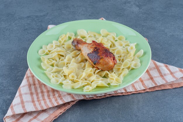 Boiled macaroni and chicken leg on green plate.