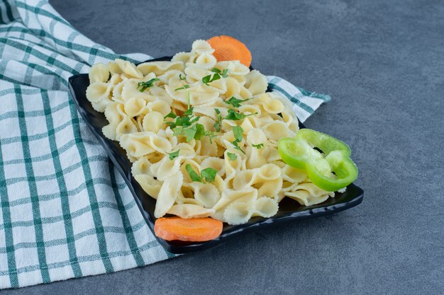 Boiled pasta with vegetables on black plate.