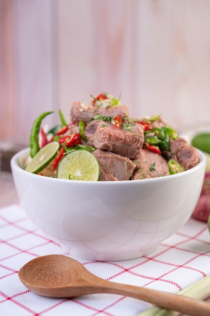 Boiled pork ribs in a white cup on a piece of fabric on a wooden table.