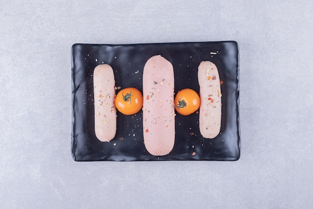 Free Photo boiled sausages and cherry tomato on black plate. 