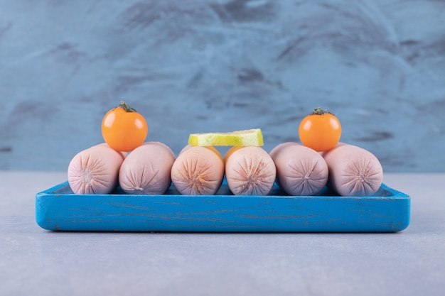 Free photo boiled sausages decorated with lemon and tomatoes on blue plate.