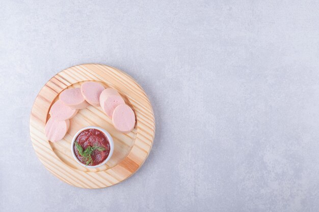 Boiled sausages and ketchup on wooden plate. 