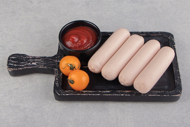 Free Photo boiled sausages with ketchup and tomatoes on black board.