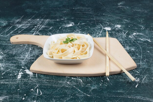 Boiled tagliatelle pasta in white bowl with chopsticks.