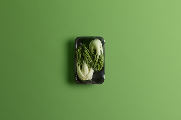 Free photo bok choy or chinese cabbage wrapped with food film on black tray. fresh vegetables for sale in supermarket isolated over green background. healthy lifestyle, refreshment and nutrition concept