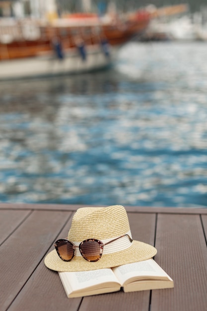 Free photo book sunglasses and a hat standing  on the shore of a port