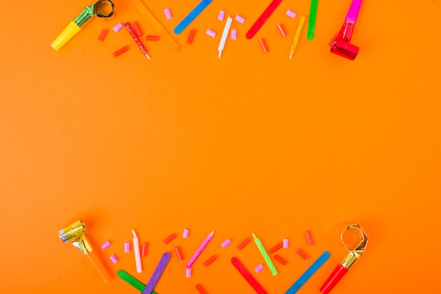 Border made with candles, candies, blowing horn and ice cream stick on an orange background