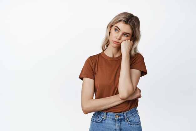 Bored and sad girl looking left lean head on fist with skeptical moody face expression standing over white background