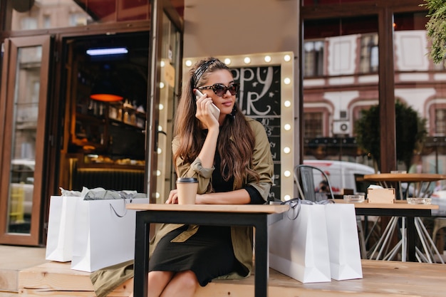 Bored woman calling someone while sitting in outdoor cafe after shopping