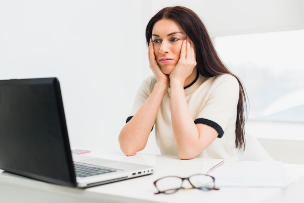 Bored woman sitting at table with laptop