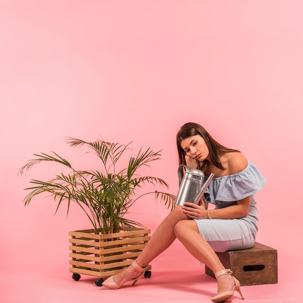 Free photo bored woman sitting with watering can near plant