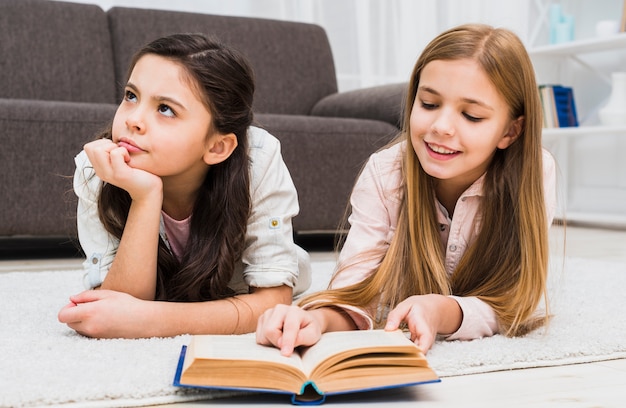 Boredom girl lying with her friend reading book in the living room