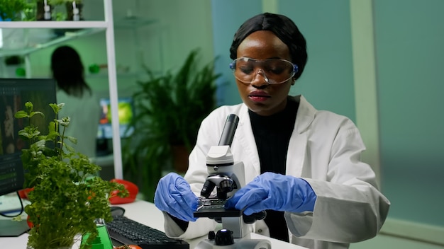 Botanist woman looking at test sample under microscope observing genetic mutation on plants