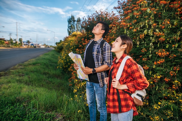 Free photo both male and female tourists carry a backpack standing at a flower garden. and look to the top