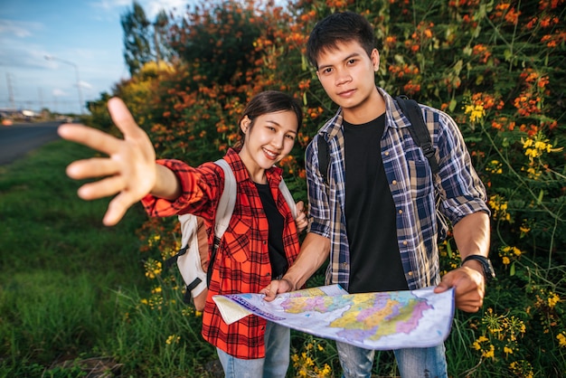 Both male and female tourists carry a backpack standing at a flower garden.