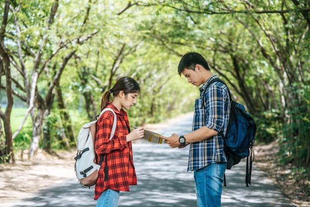 Both male and female tourists stand to see the map on the road.